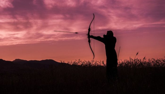 A bowhunter using a traditional style bow in the evening.